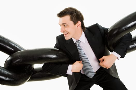Portrait of powerful businessman holding two sections of huge chain by arms over white background