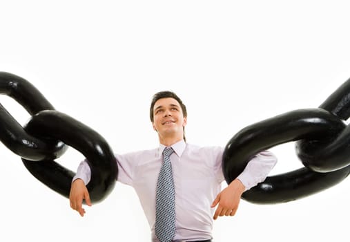 Portrait of powerful businessman holding two sections of huge chain by arms and looking upwards with smile over white background