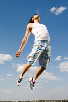 Image of energetic man jumping high against bright blue sky