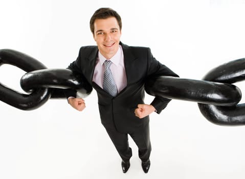 Portrait of powerful businessman holding two sections of huge chain by arms over white background