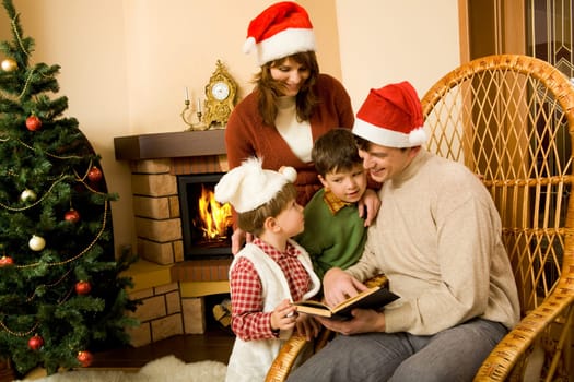 Portrait of smiling man with book in hand sitting in rocking-chair and looking at his little sons standing near by