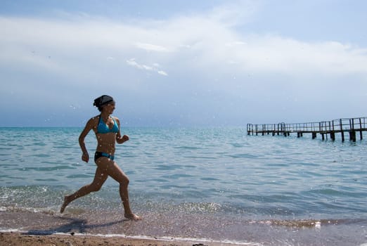 Photo of energetic female in swimsuit running along seashore during summer vacations