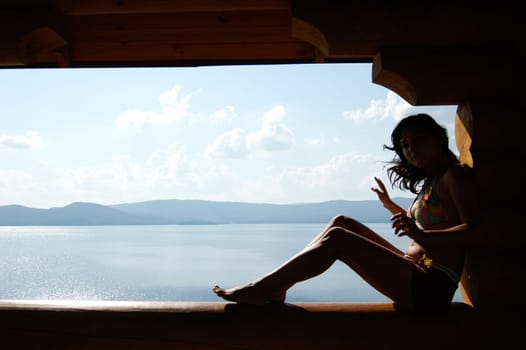 Pretty woman sitting on wood and pointing at nice lake surrounded by mountains