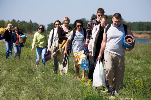 Image of queue of tourists walking down green grass while on trip outdoors