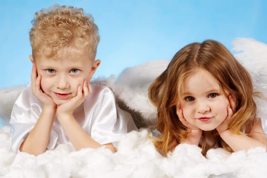 Small boy and girl in angelic costume lying on white cloud