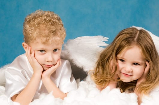 Photo of small boy and girl in angel dresses lying on white cloud and having rest