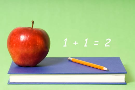book and apple and pencil on green