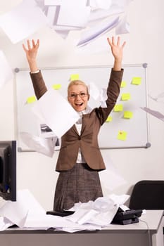 Portrait of happy businesswoman raising arms and throwing papers in office with laugh