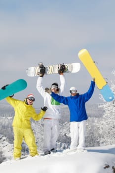Portrait of joyful three snowboarders raising their boards