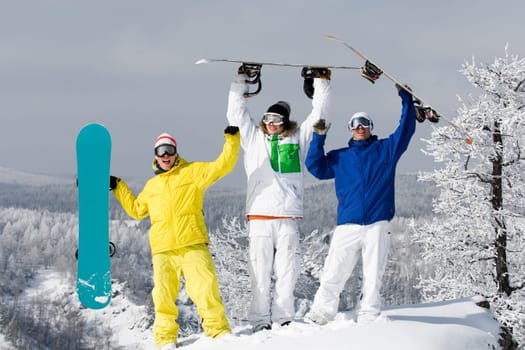 Portrait of three happy young men with snowboards raising their arms