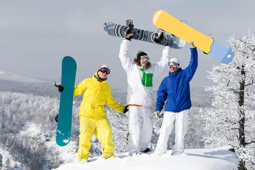 Portrait of three successful snowboarders raising their arms