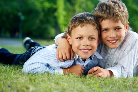 Portrait of happy boys lying on green grass and smiling at camera