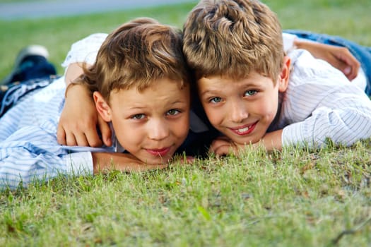 Portrait of happy boys lying on green grass and smiling at camera