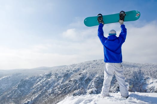 Rear view of sportsman with snowboard standing on top of mount