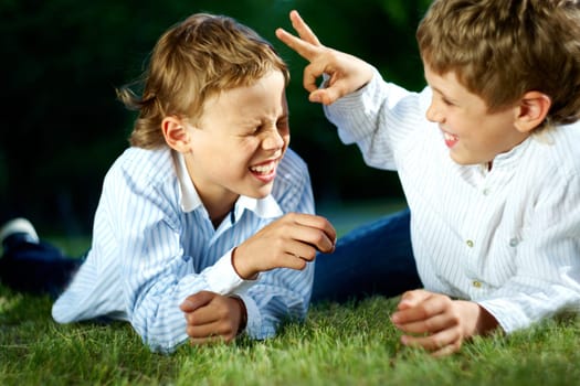 Portrait of happy boys playing jokes on grass in park