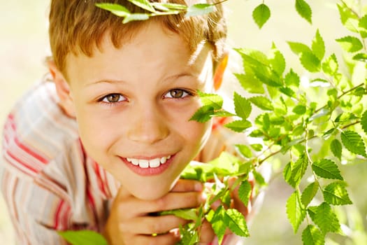Portrait of handsome schoolboy smiling at camera out of green branch