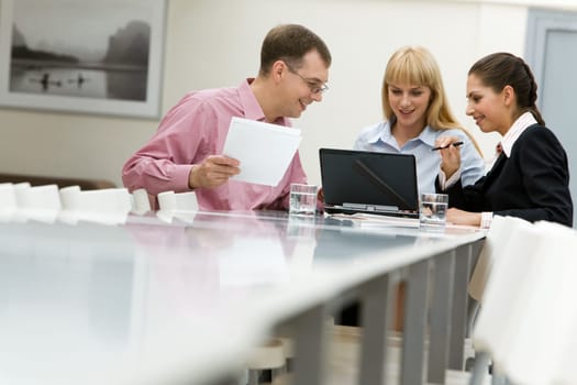 Image of business group communicating at the table and looking at laptop monitor in workshop