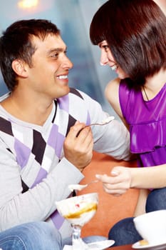 Happy girl and handsome man looking at each other while eating ice-cream in cafe