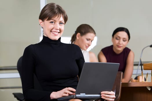 Portrait of smiling woman with the laptop on her knees sitting in the cafe and two girls on the background