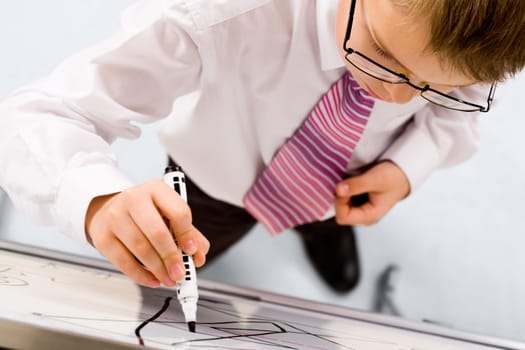 Smart boy with pen in hand standing by whiteboard and writing on it