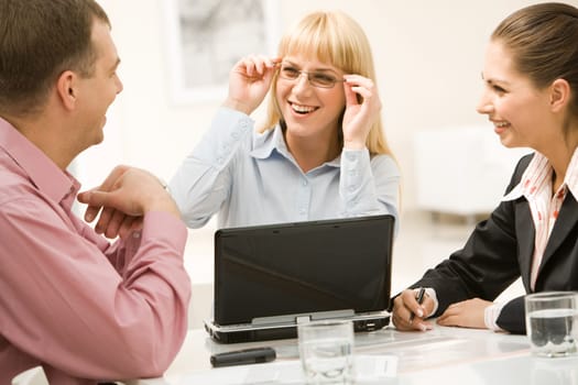 Portrait of joyful woman wearing glasses and looking at business partners who smiling at her