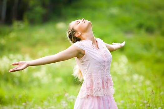 Photo of relaxing woman with closed eyes and stretched arms expressing delight outdoors