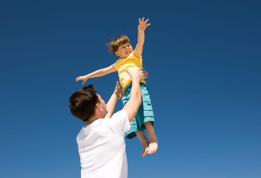 Photo of happy man raising his cute son against bright blue sky