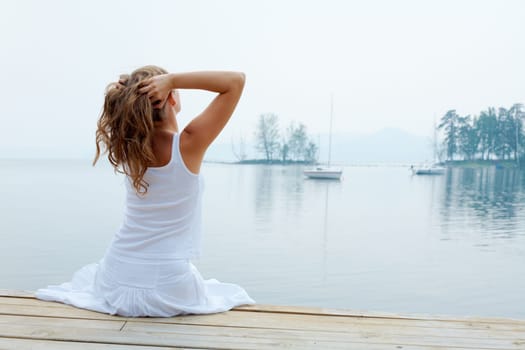 Rear view of pretty young lady in white cotton clothes having rest by the seaside