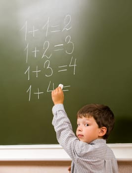 Portrait of pensive schoolchild standing at blackboard and doing sums