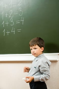 Portrait of pensive schoolchild standing at blackboard and doing sums