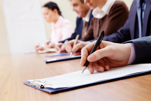 Row of business people making notes with focus on hand holding pen