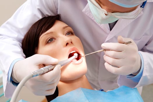 Image of young woman keeping her mouth open while dentist examining it
