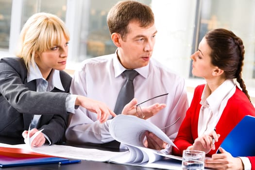 Image of a business lady looking attentively at the speaking business leader while the other woman pointing at some details in the document