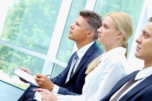Row of three smart employees writing at conference
