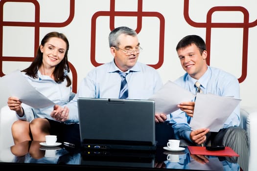 Adult businessman sitting at the table and giving documents to managers