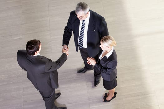 Senior manager shaking hands with his partner, their colleague clapping