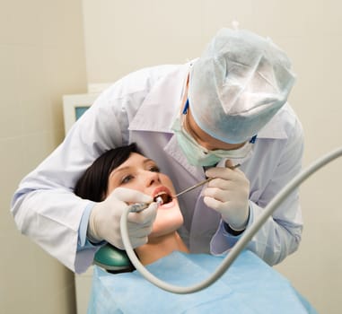 Photo of dentist in uniform examining oral cavity of young female patient