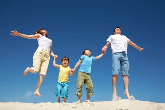 Photo of happy parents holding their son by hands in jump with bright blue sky at background