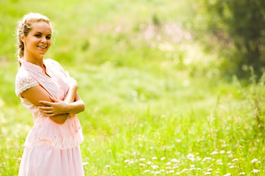 Portrait of smiling girl standing with her arms crossed on chest and looking at camera on background of green field