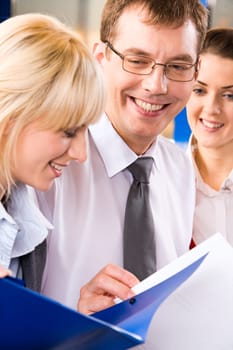 Image of two business ladies and a businessman reading and discussing business plans happily smiling