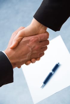 2 hands shaking with a blank contract and pen