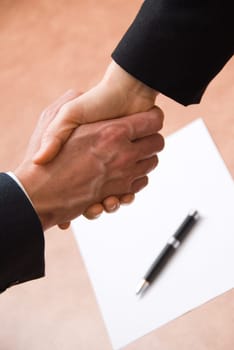2 hands shaking with a blank contract and pen
