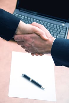 2 hands shaking with a blank contract and pen
