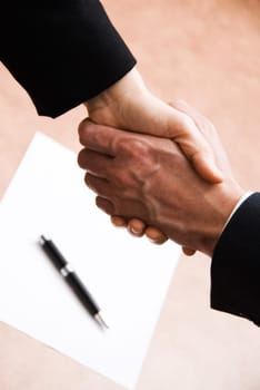 2 hands shaking with a blank contract and pen