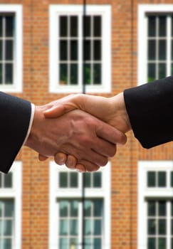 business hand shake in front of a brick building
