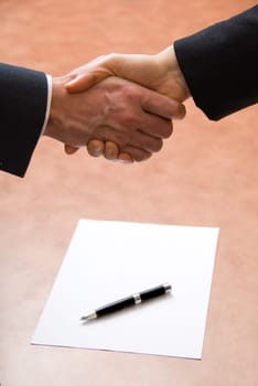 2 hands shaking with a blank contract and pen