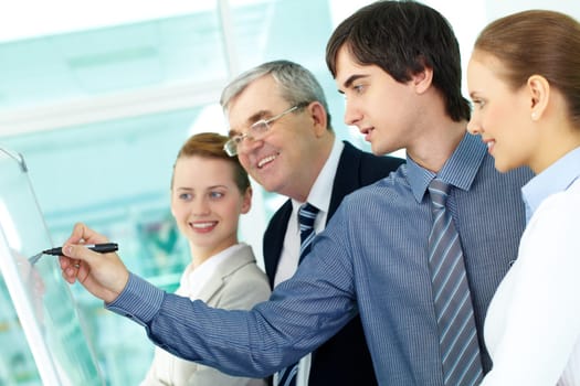 A business man writing on whiteboard with a highlighter while explaining something to colleagues
