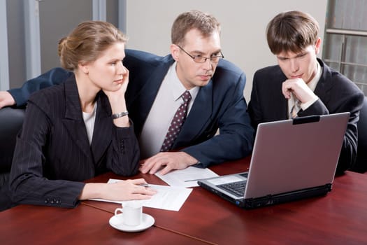 Business team of three professionals looking at monitor of laptop in the office