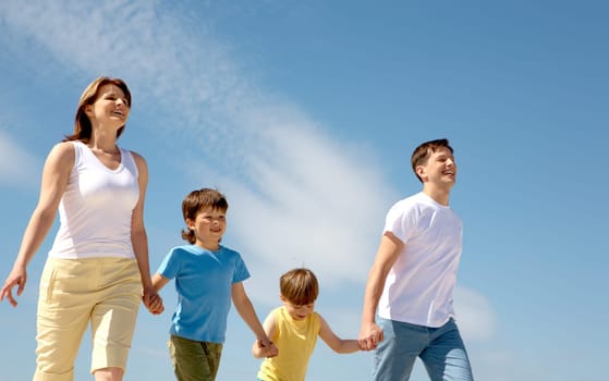 Photo of happy parents holding their sons by hands with bright blue sky at background
