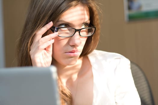 Portrait of pretty employee looking aside through eyeglasses and touching them